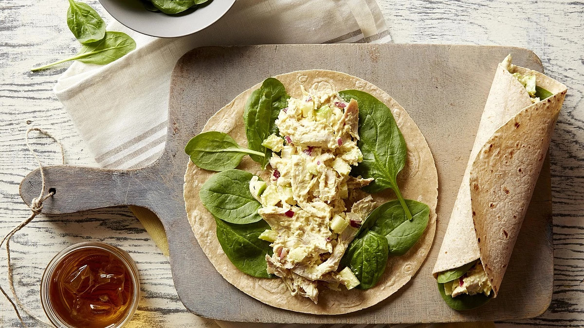 An overhead view of curried chicken and apple wraps on a cutting board