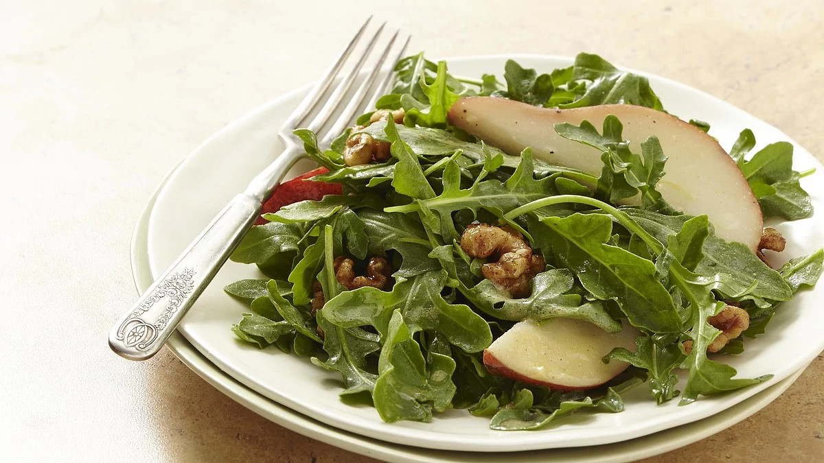 A close-up view of pear and arugula salad with candied walnuts on a plate