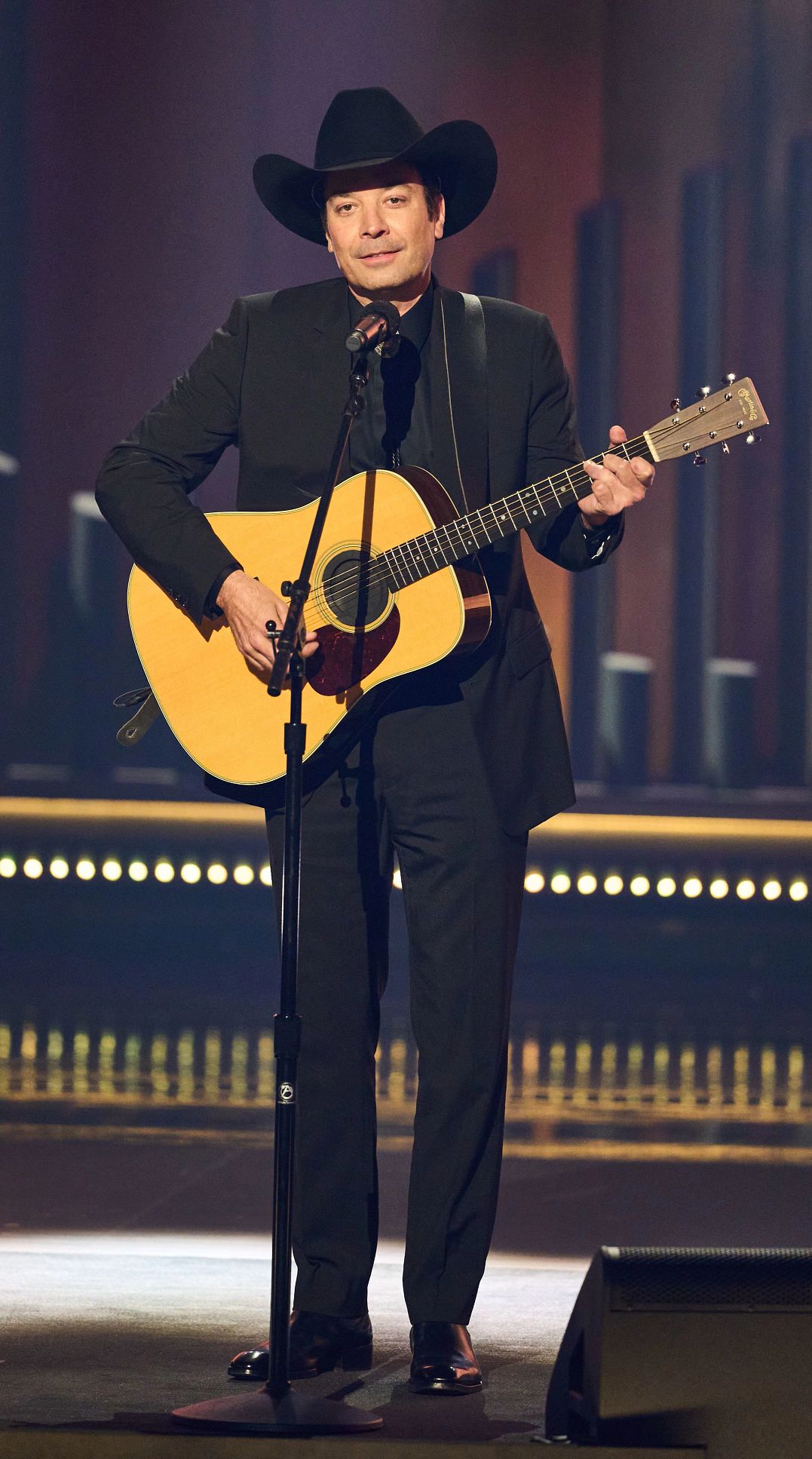Jimmy Fallon wearing a country hat and playing an acoustic guitar onstage at the 25th Annual Mark Twain Prize For American Humor