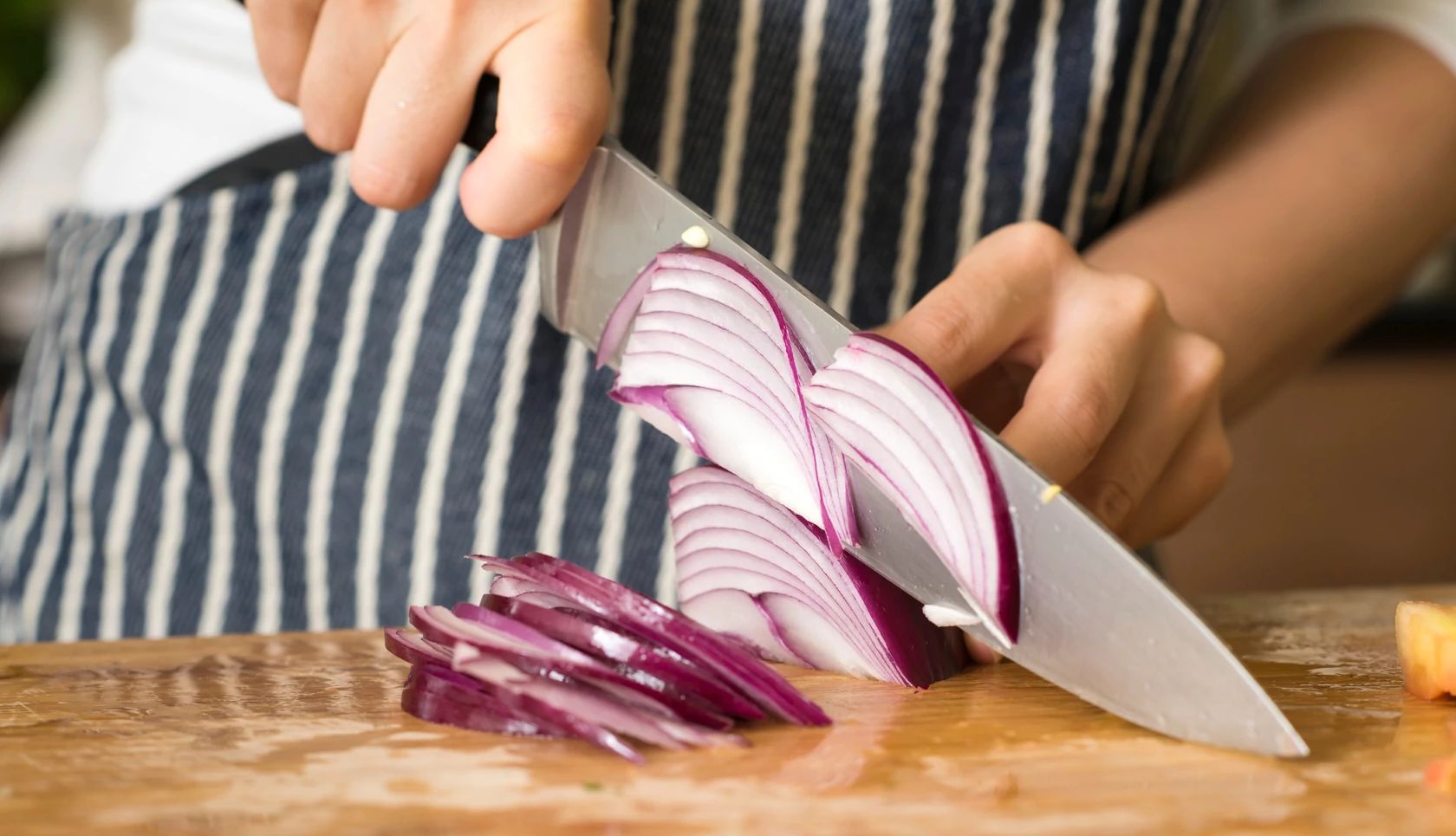 How to Cut Onions Without Crying a close-up of a person cutting a red onion