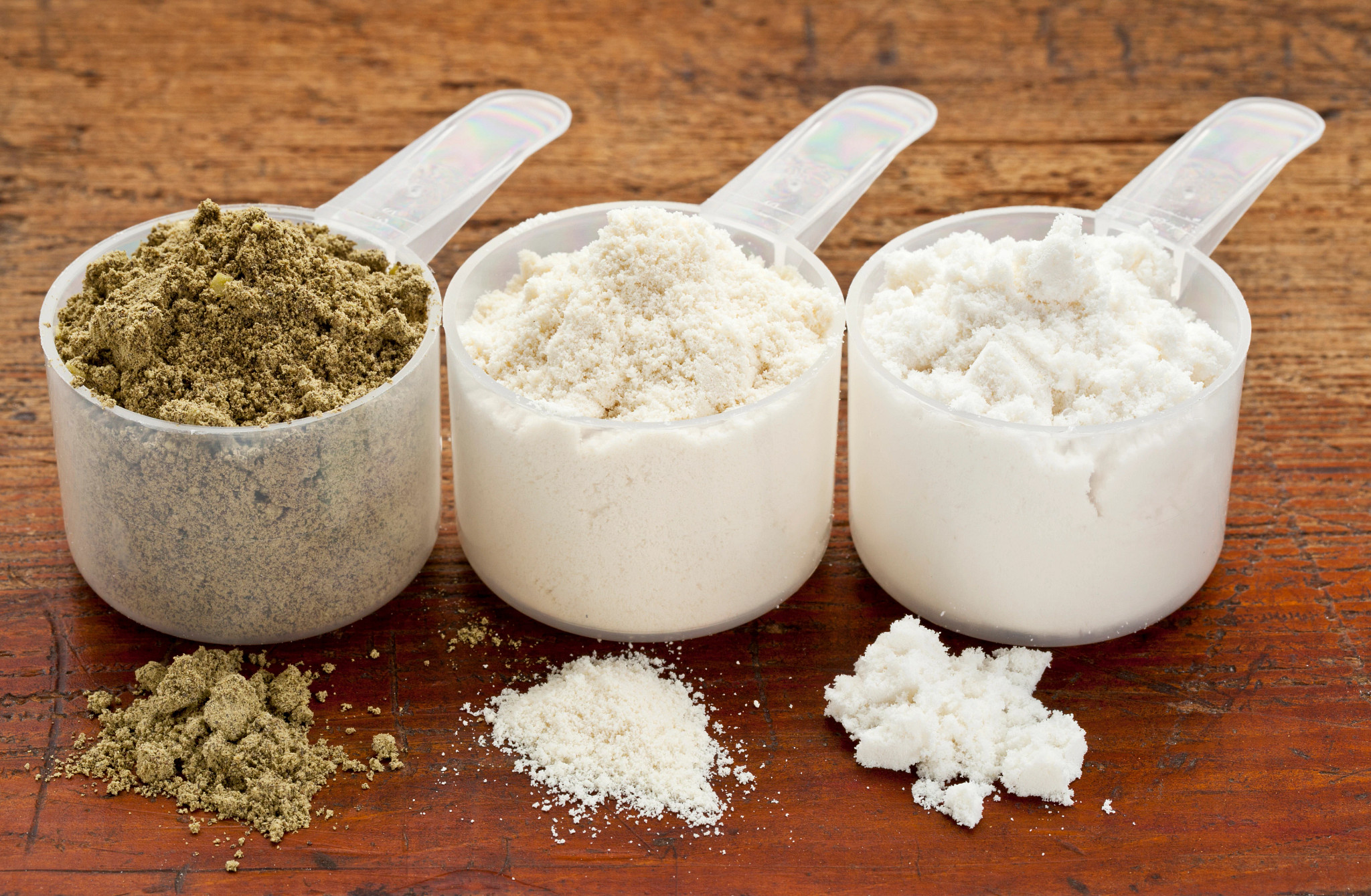 Three scoops of protein powder on a wooden table