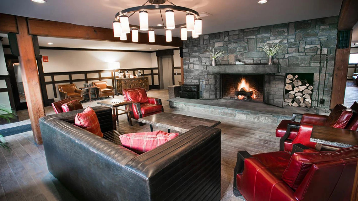 BW Signature Collection® by Best Western winter ski resort lodge lounge area with leather couch and chairs, fireplace, stacked wood, large circle chandelier, stone and wood accents