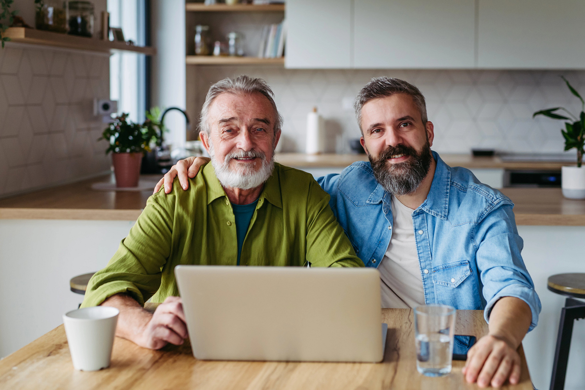 Mature son helping father to manage his finance, teaching how to work with internet baking and shopping online. Handsome son supporting dad, technology and digital literacy.