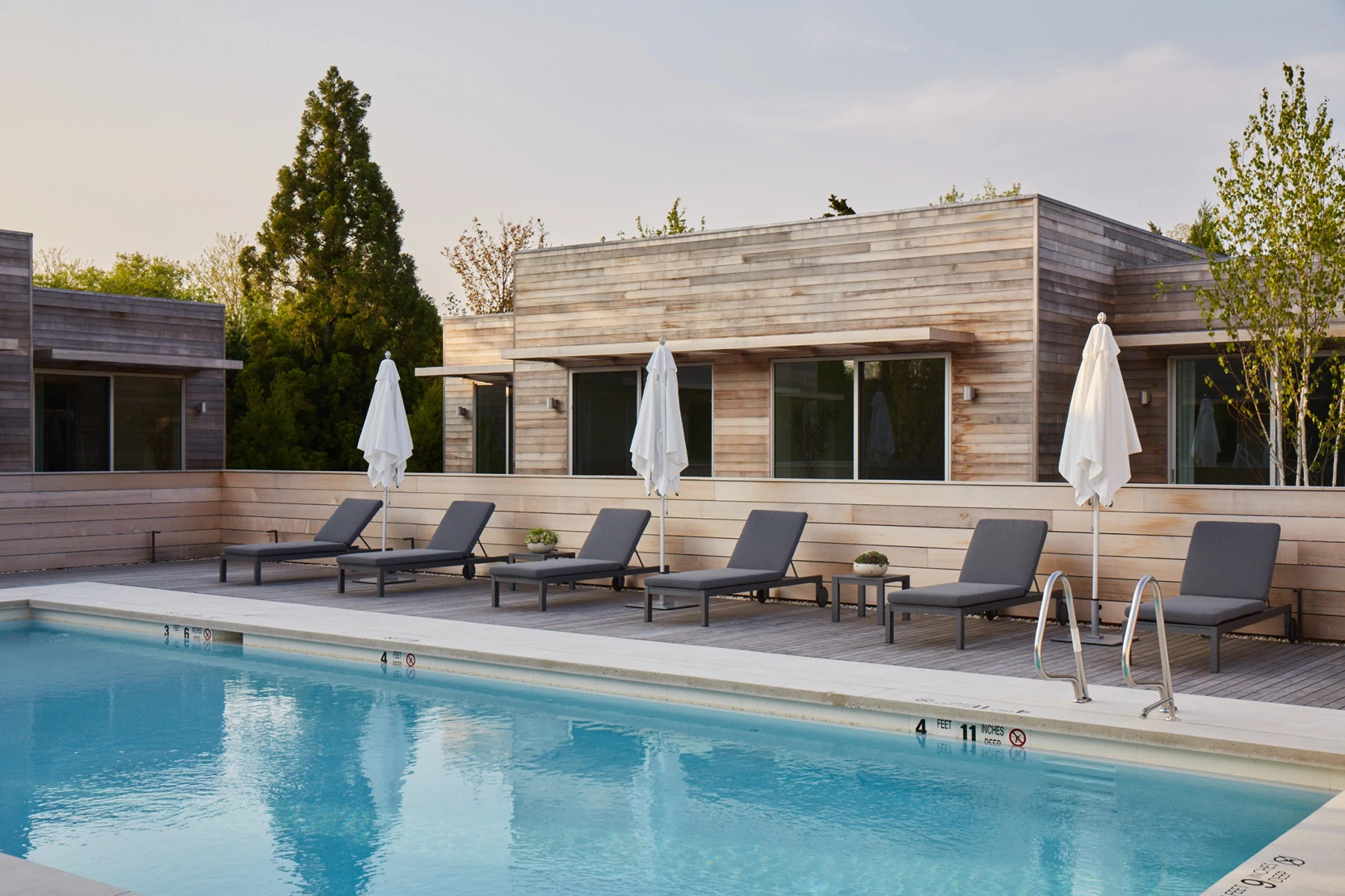 Contemporary pool area with lounge chairs and resort buildings surrounded by trees