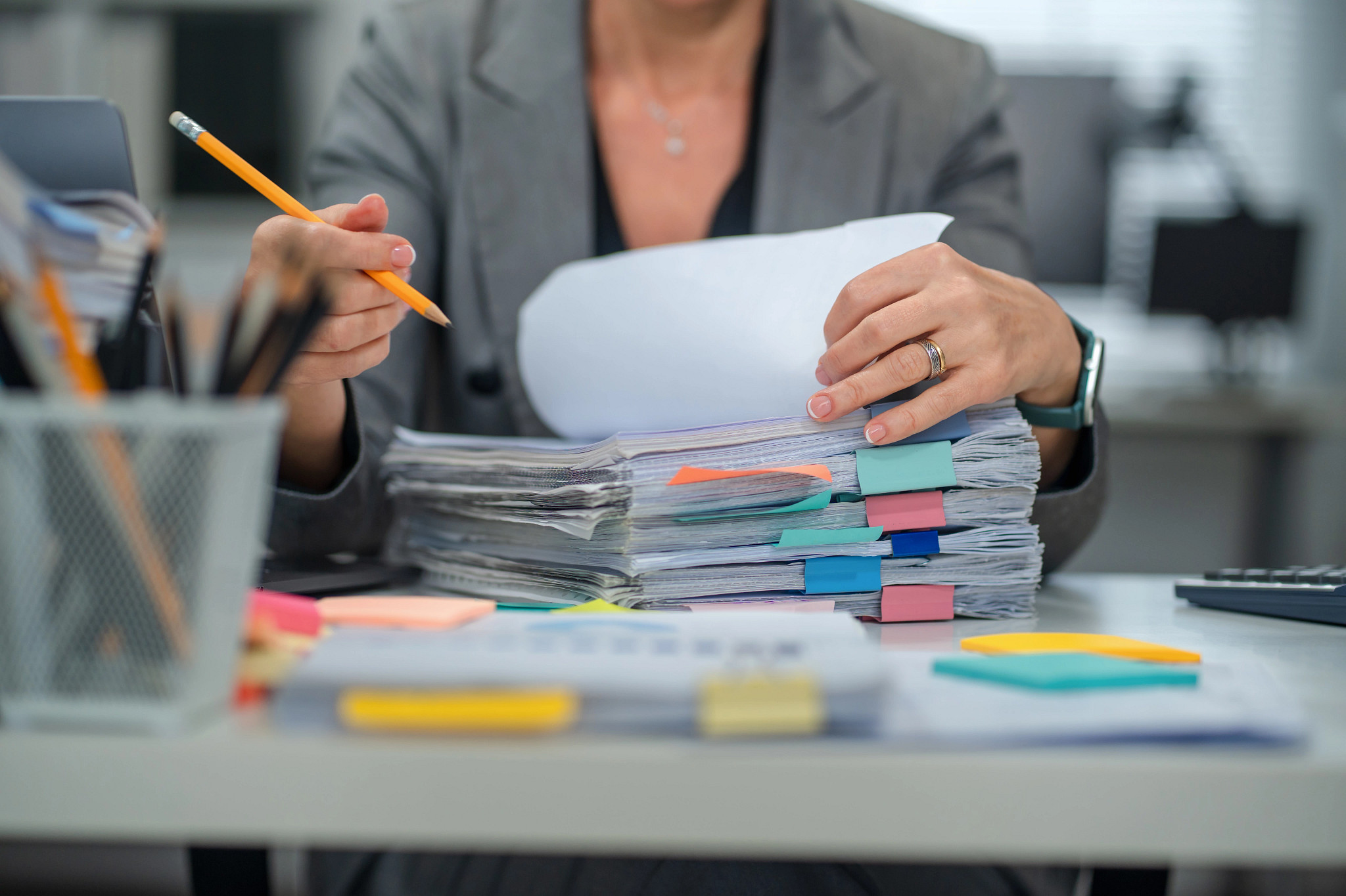 A photo shows an older adult woman working through a stack of papers, making notes with a pencil