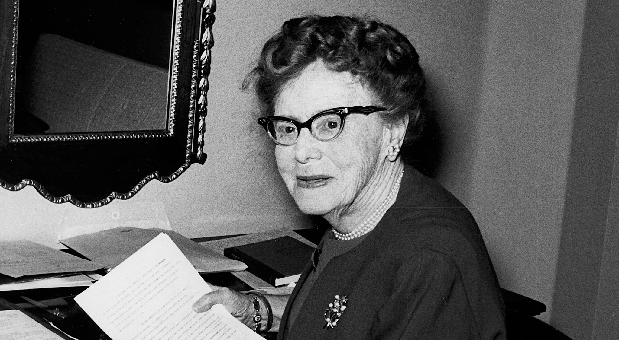 Image of Dr. Ethel Percy Andrus, black and white image of her at her desk with some papers. She is smiling and facing the camera