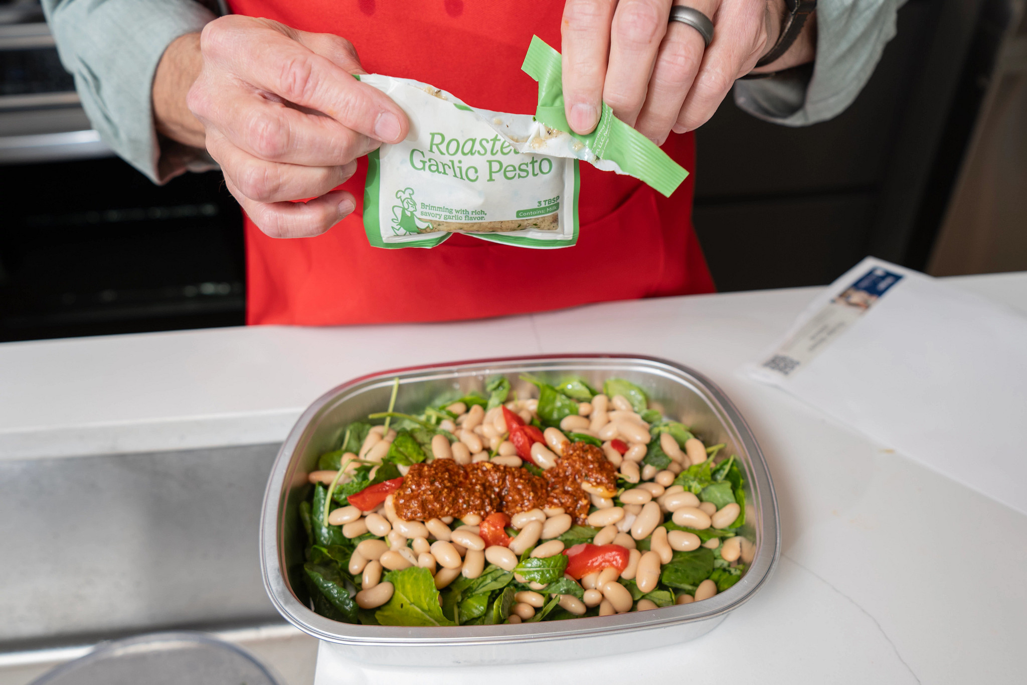 A person opening an ingredient pouch above a Blue Apron meal on the counter
