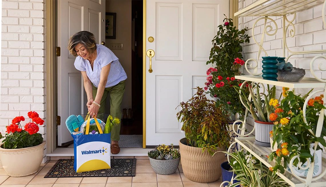Walmart Plus Woman collecting her Walmart Plus delivery bag off the porch of her home with potted plants decorating the patio