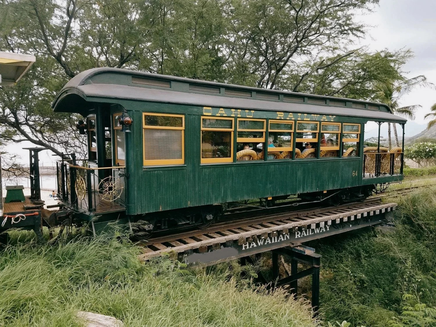 Vintage green Hawaiian Railway parlor car on a coastal rail line surrounded by tropical trees