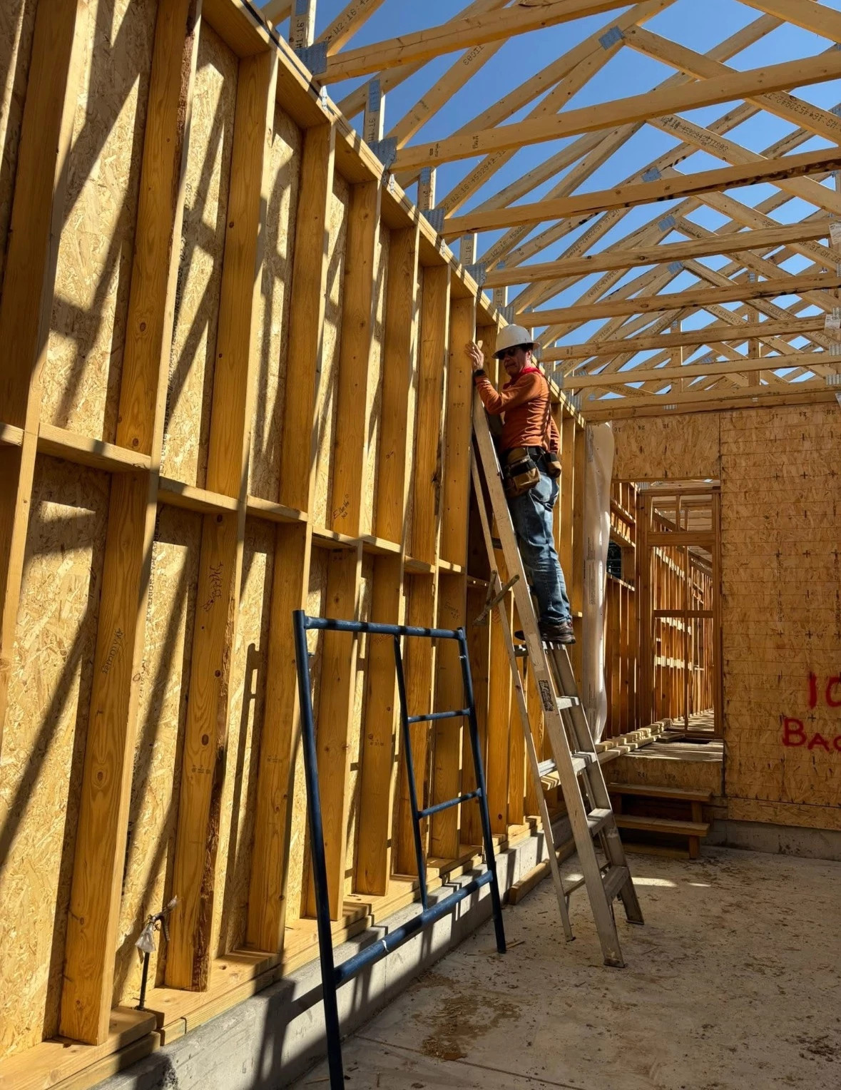 a photo shows Peter Moore on a ladder at Habitat for Humanity build in Colorado, helping install structural metal connectors, known as hurricane ties