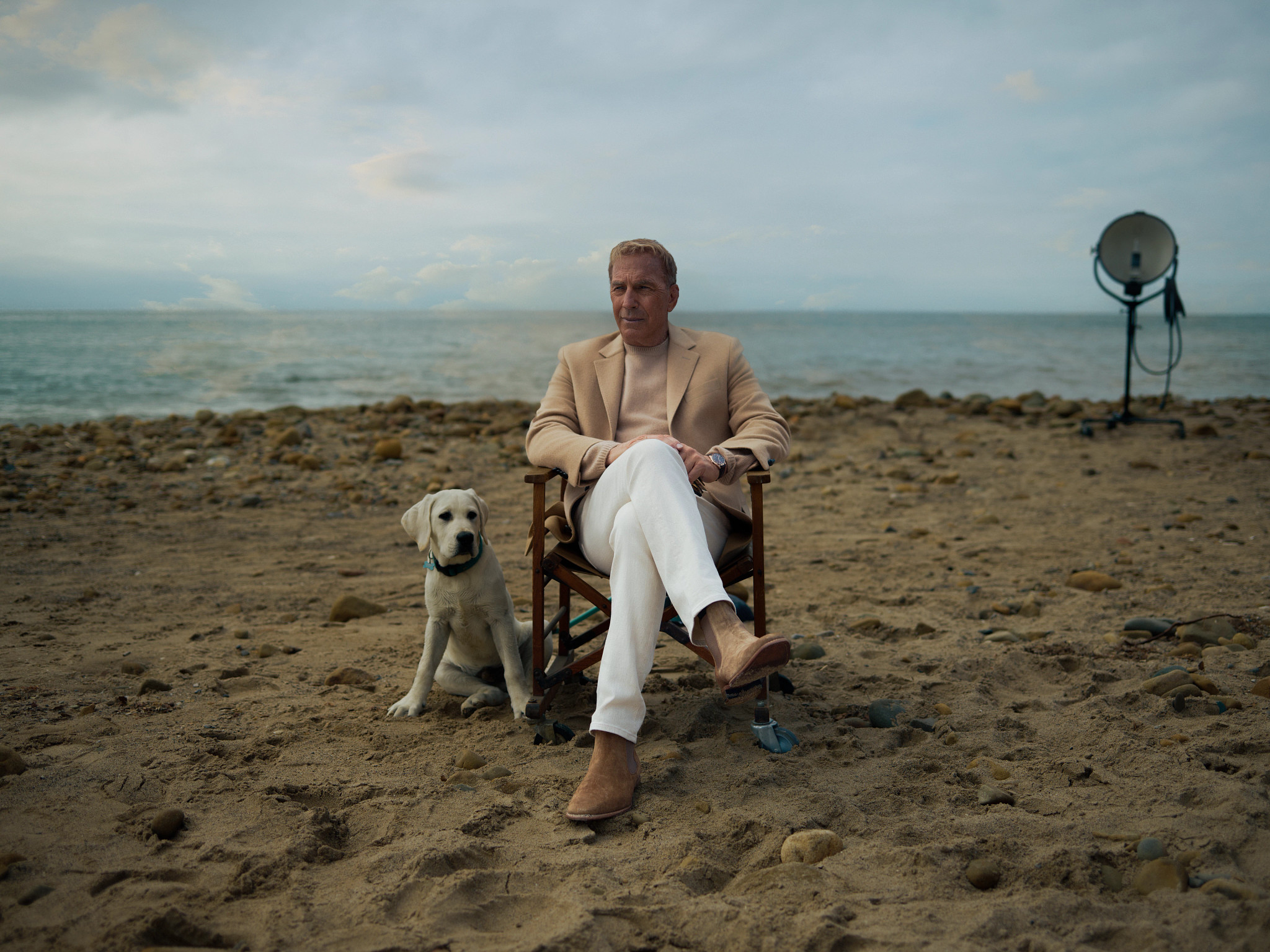 Kevin Costner sentado junto a un perro con el mar de fondo