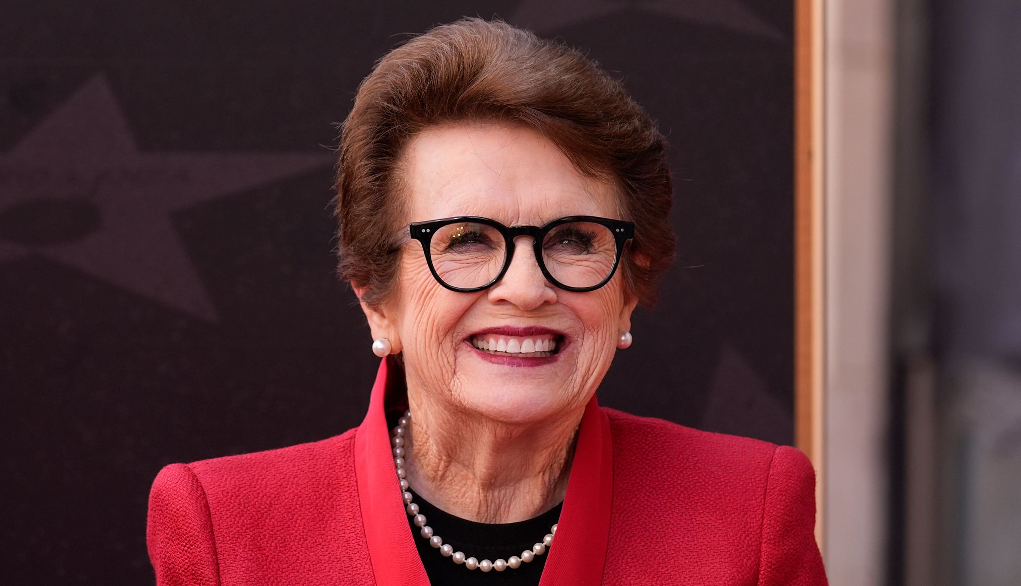 Billie Jean King Back in School billie jean king smiling, wearing a red jacket and glasses
