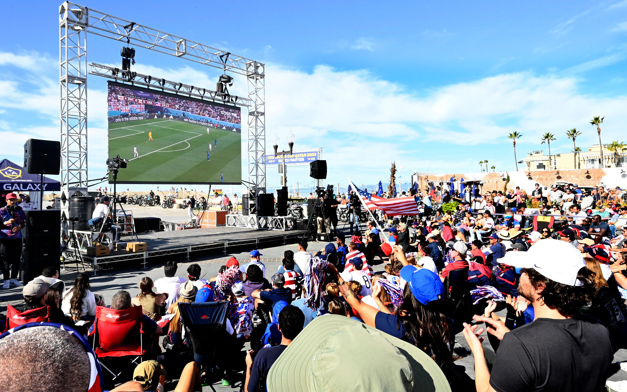 people cheering and waving american flags as they watch a world cup soccer match on a large screen outdoors