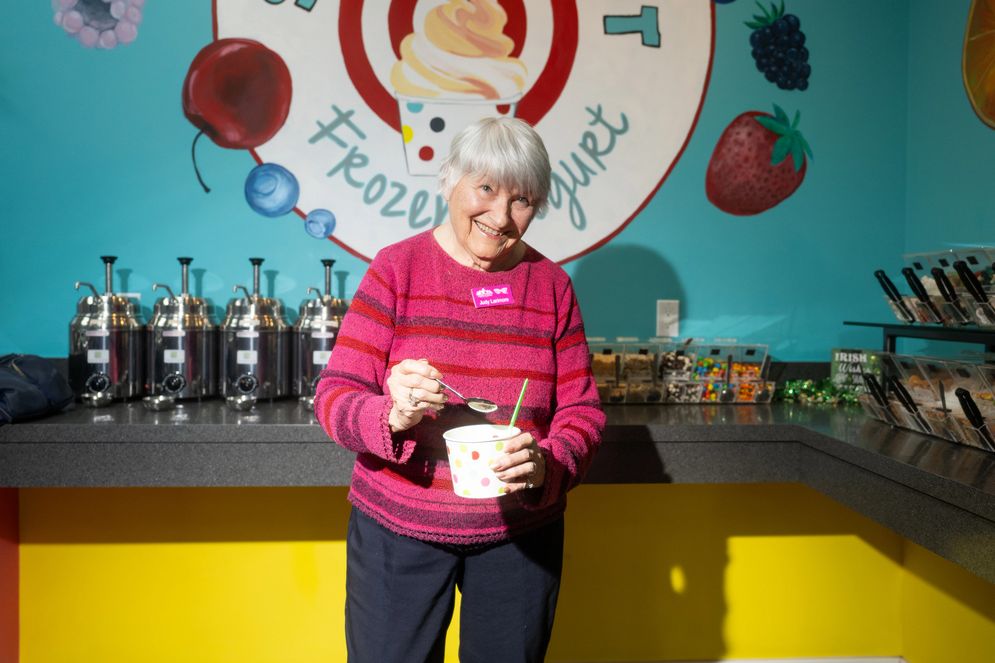 an older woman smiling, holding a paper dessert cup