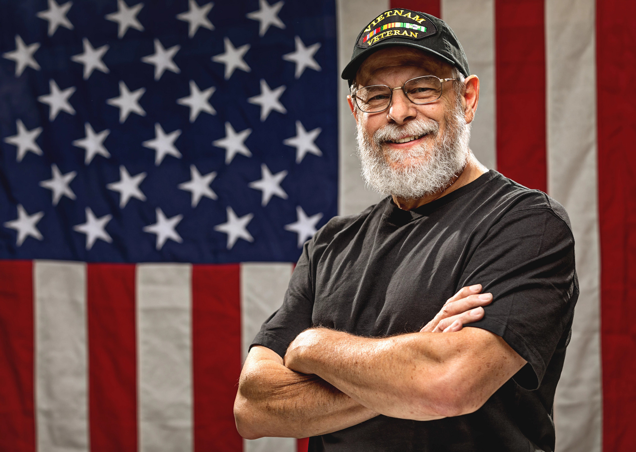 veteran standing in front of an American Flag with arms crossed