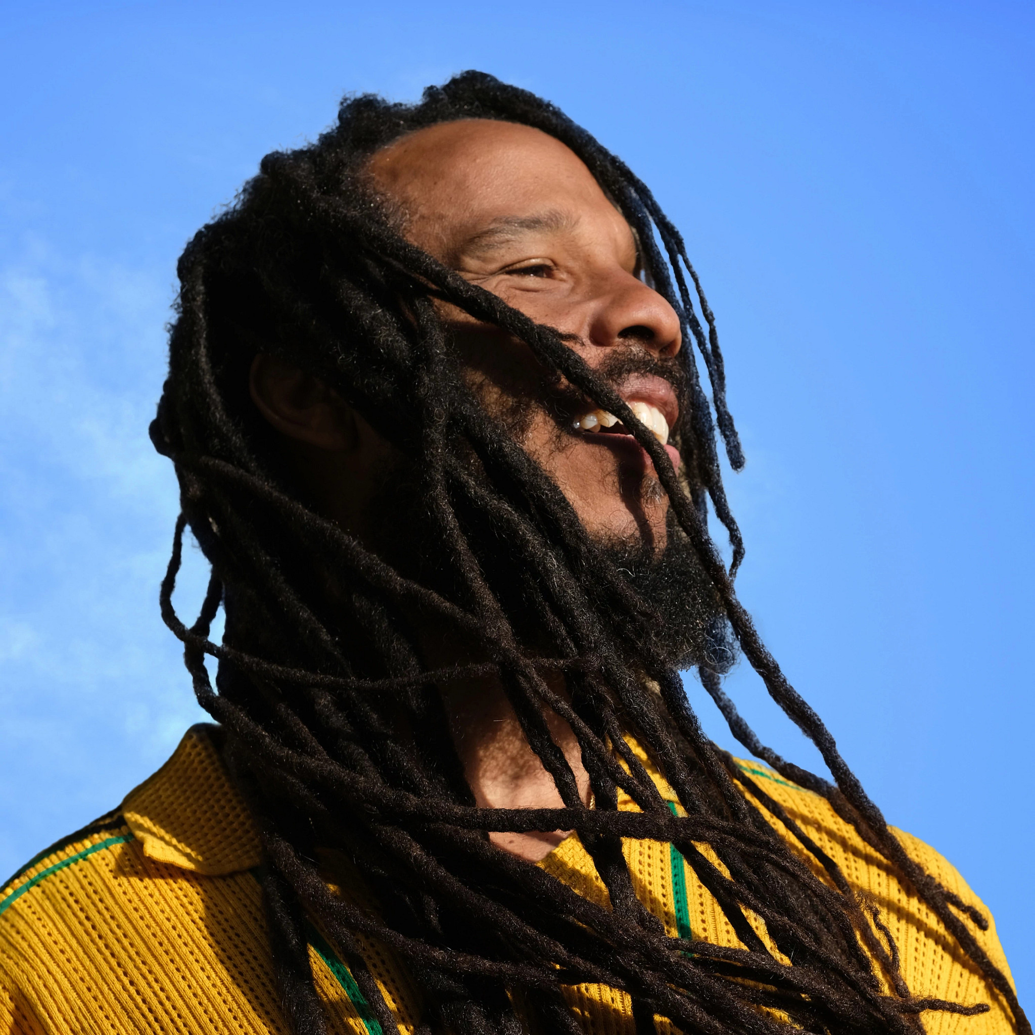 ziggy marley posing for a close portrait with a bright blue sky in the background