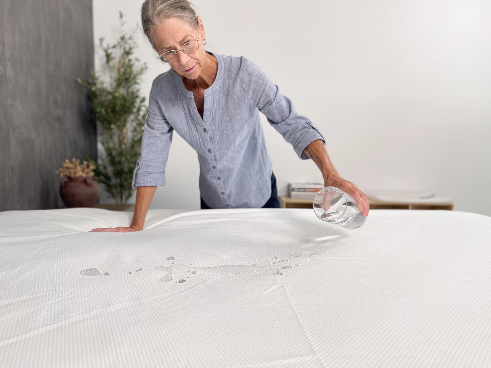 A woman pours water from a glass onto a mattress protector