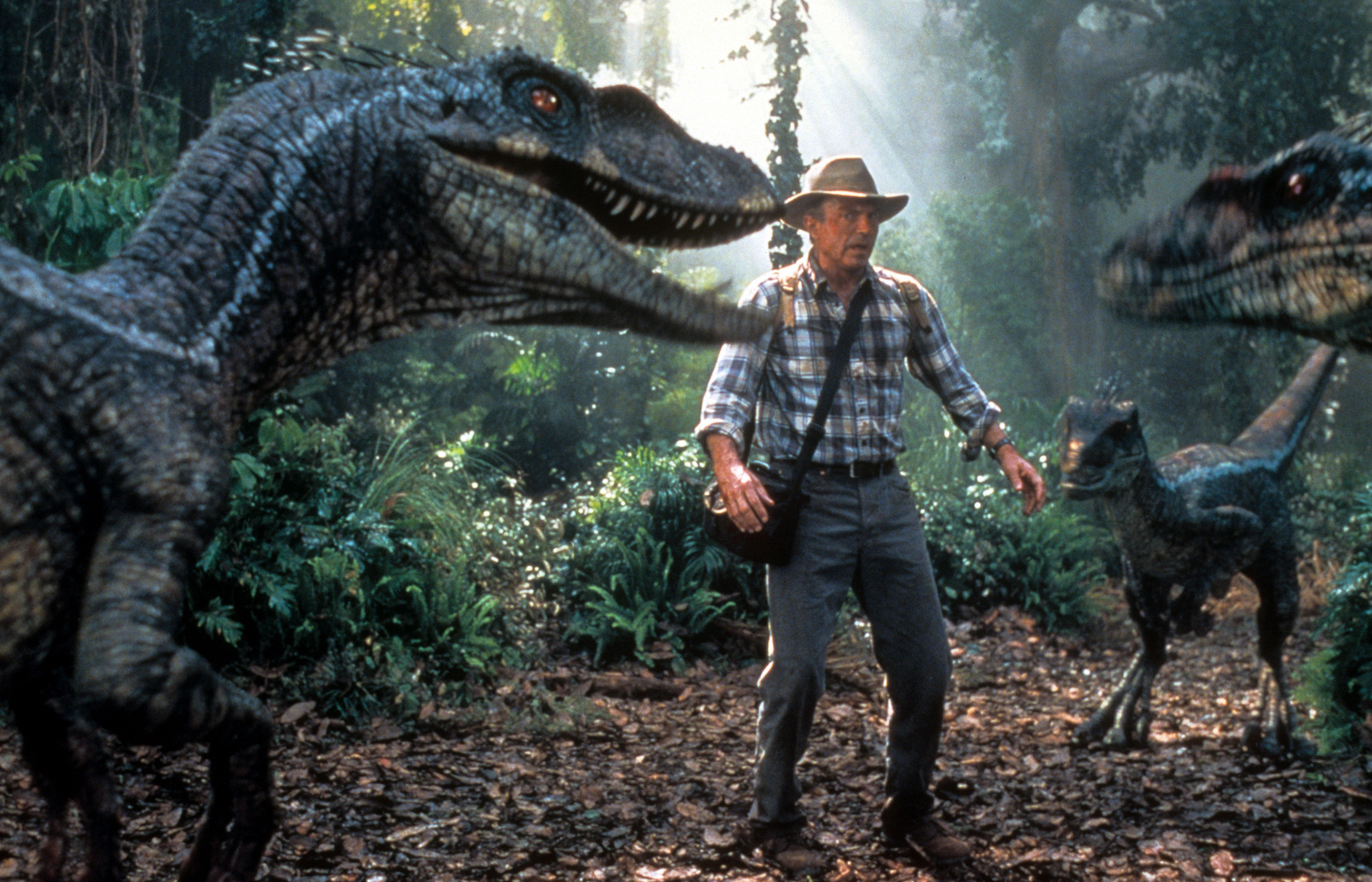 sam neill surrounded by three dinosaurs