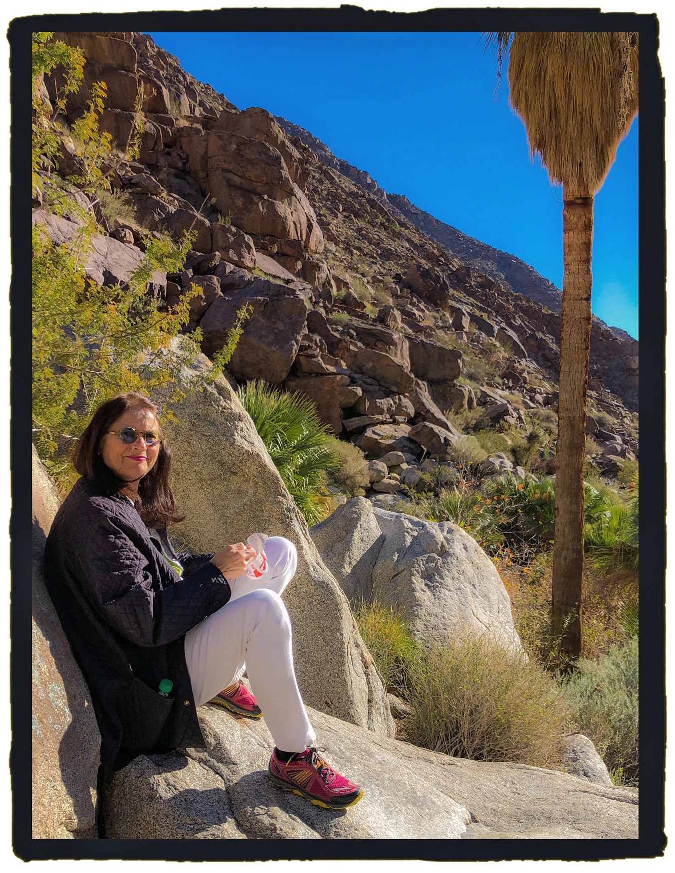Rebecca Cross seated on a large rock during a canyon hike in a desert landscape.