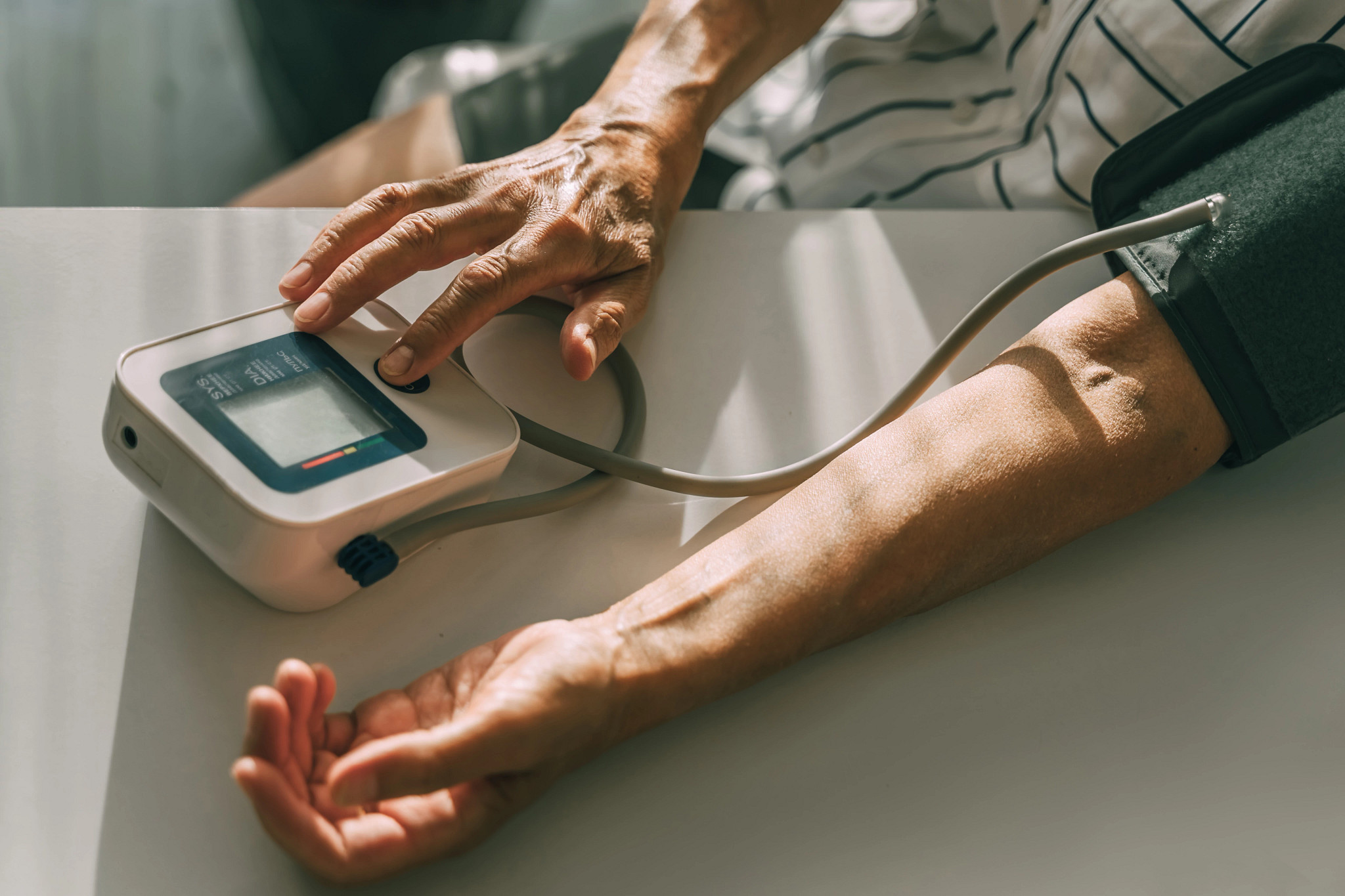 Close-up of an older adult using a digital blood pressure monitor on their arm resting on a table.