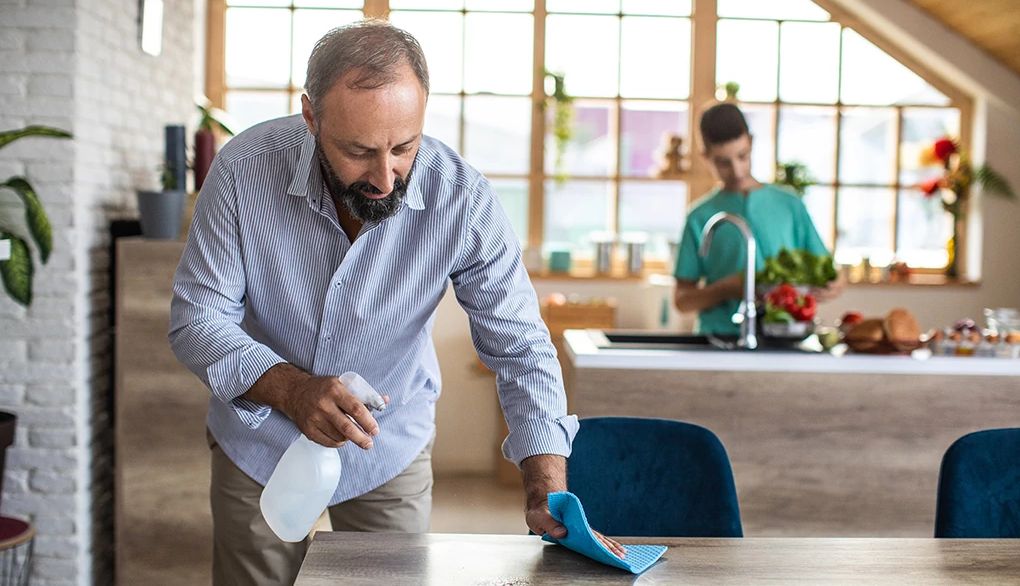Turn chores into a healthy workout A man using a spray bottle and rag to clean a table