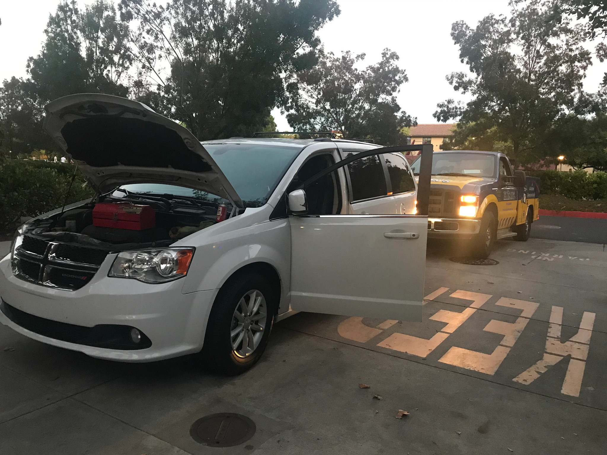 White van with front hood and driver's side door open; black and yellow pickup truck behind it