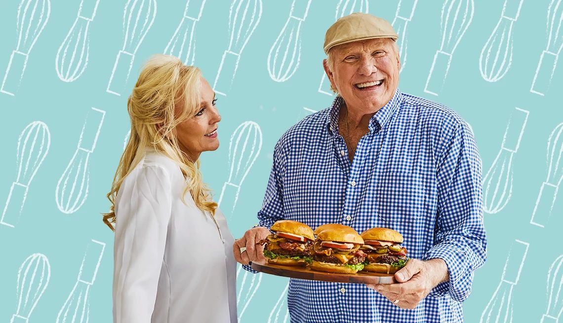 Bradshaw Family Cookbook A photo shows football legend Terry Bradshaw and his wife Tammy in front of a blue backdrop. Terry is holding a platter of burgers
