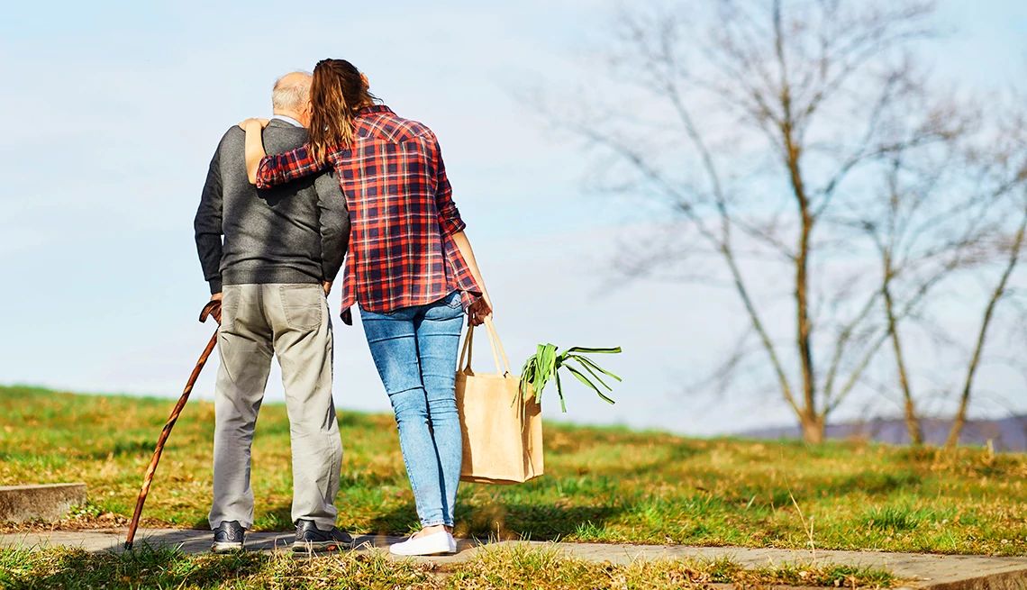 An AARP-backed bill aims to encourage employers to offer paid leave for caregiving A woman holding a grocery bag puts her arm around an older man with a cane