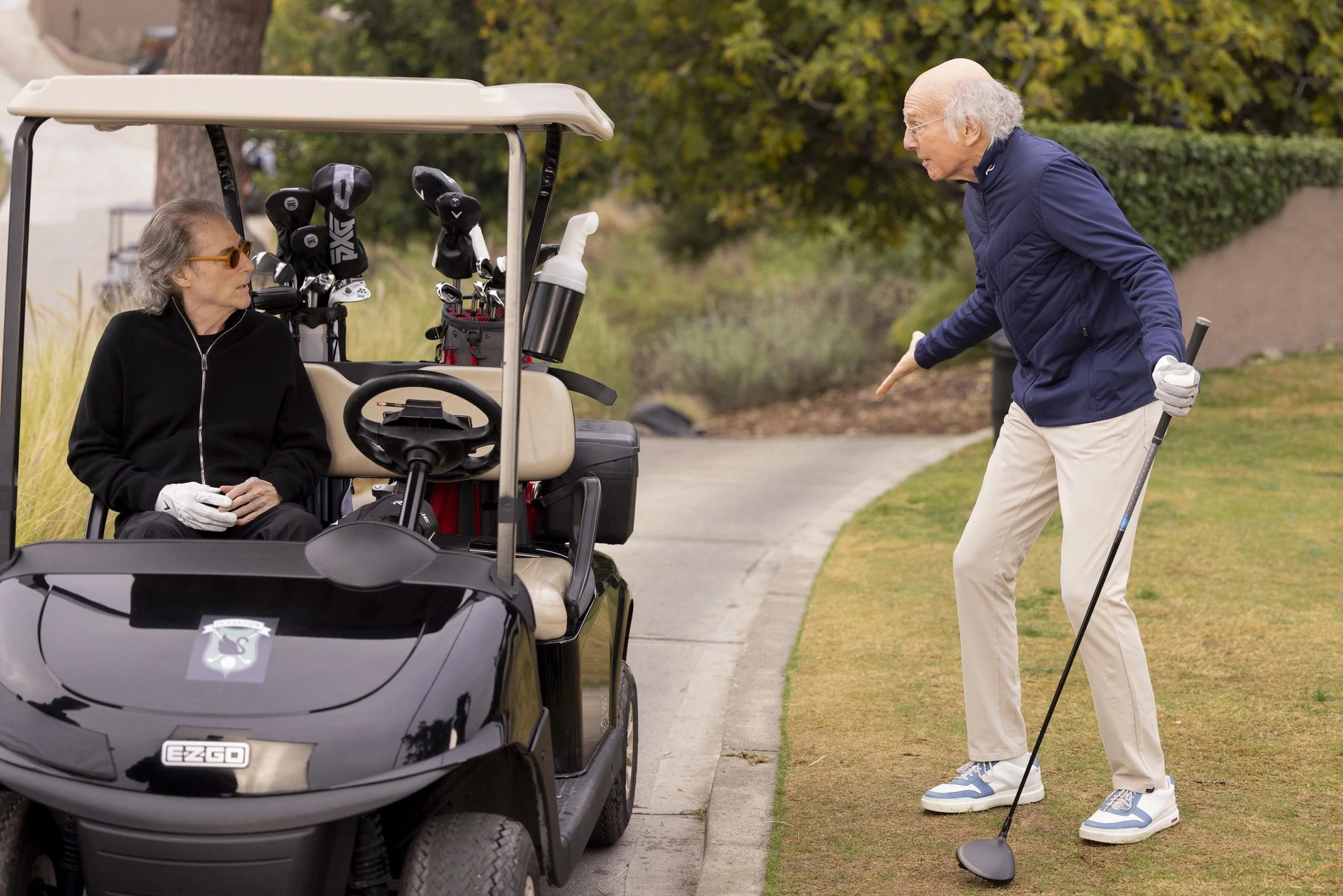 Richard Lewis sitting in a golf cart and Larry David holding a gold club in "Curb Your Enthusiasm."