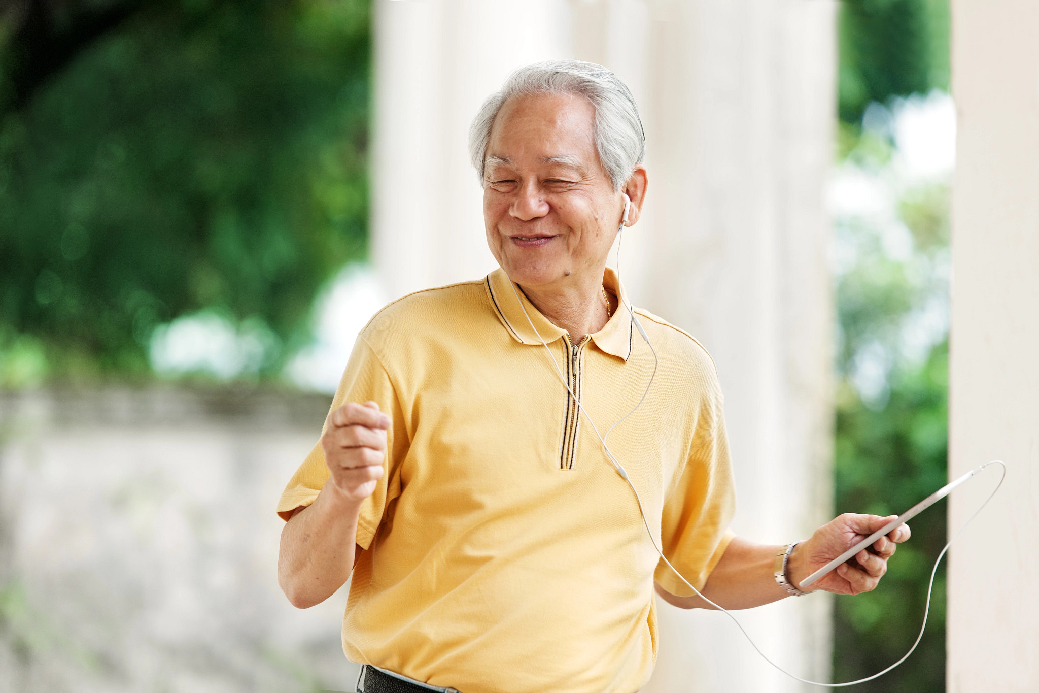 A man with earbuds in his ears listening and dancing to music with a tablet in his hand