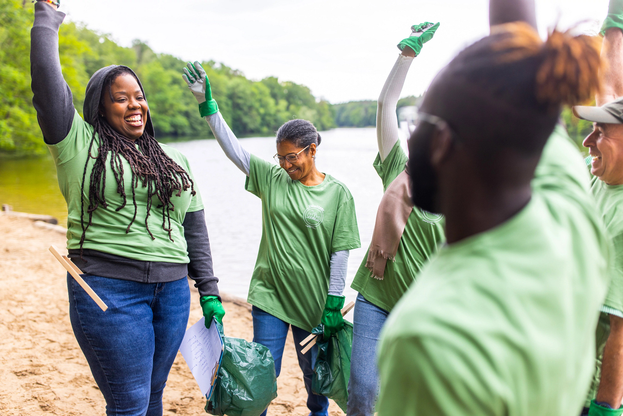 Group of volunteers cheering and showing unity while cleaning the beach along the lake