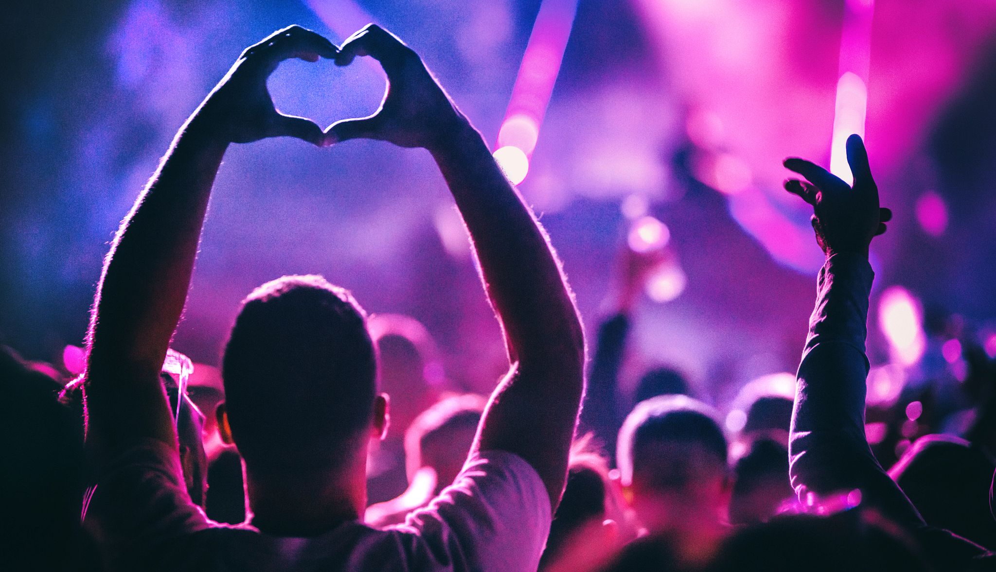 Closeup rear view of group of people at a concert party. One person is showing heart symbol with their hands Closeup rear view of group of people at a concert party. One person is showing heart symbol with their hands