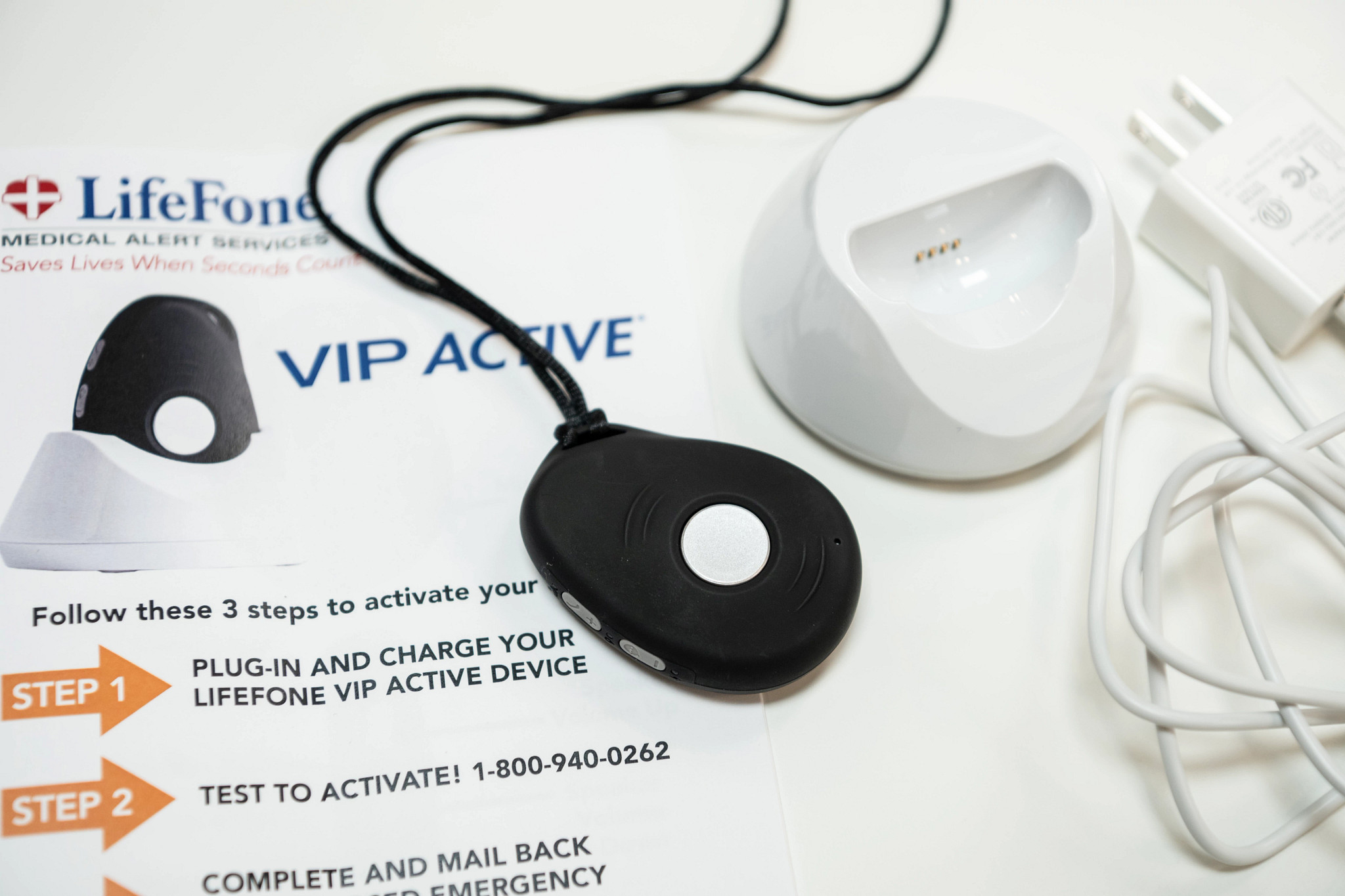 The Lifefone VIP Active on top of a white table and its manual alongside its charging port