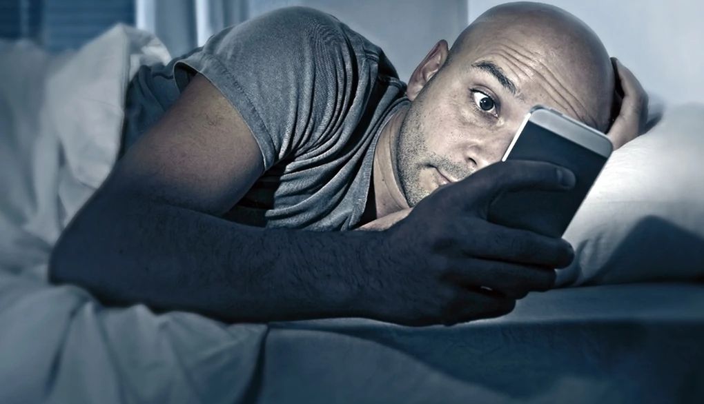 The light from electronic devices may interfere with sleep patterns A man looking at his phone while in bed
