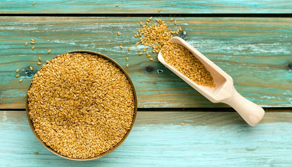 Sprinkling flaxseed on your meals may provide a nutrient boost A bowl of golden linseed and shovel on green wood