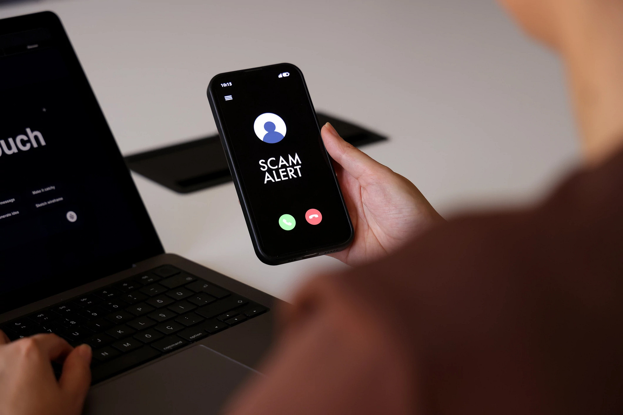 A person holds a smartphone displaying a “Scam Alert” message on an incoming call screen. The dark interface clearly indicates a fraud warning, conveying concerns about cybersecurity, mobile fraud, and digital safety. The indoor environment and close-up composition highlight the immediacy and relevance of online threat awareness in everyday mobile use.
