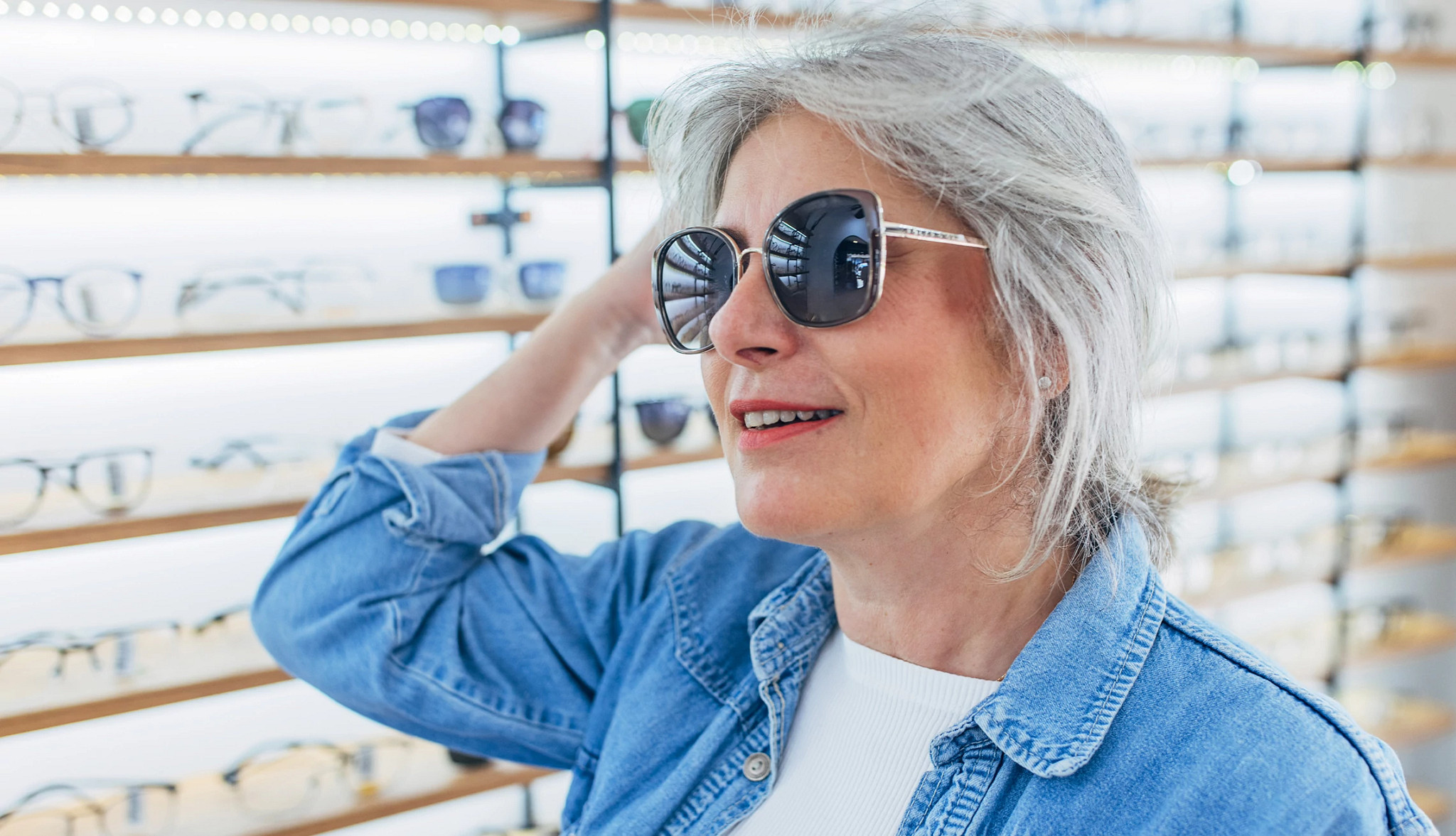 an older person trying on a pair of stylish oversized sunglasses inside an eyewear shop