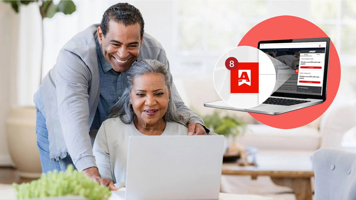 AARP Perks™ Browser Extension man standing behind woman sitting looking over her shoulder smiling as the both look at an open laptop, in corner laptop open over red circle, magnifying the extension on screen notification symbol