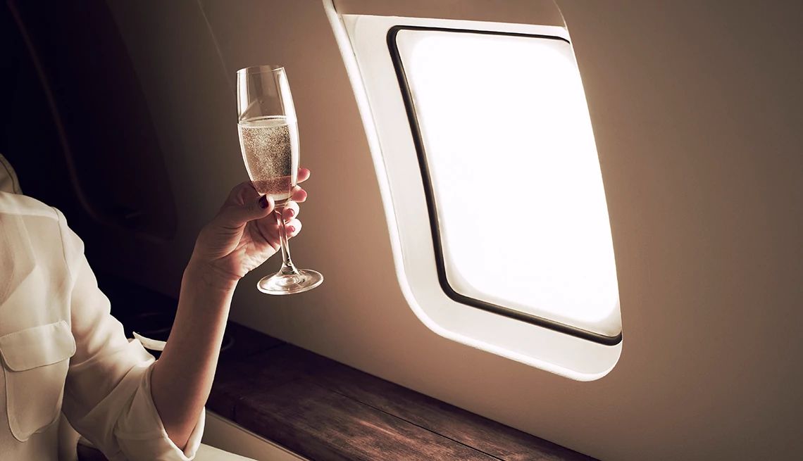 Should You Drink on an Airplane? person on plane with champagne