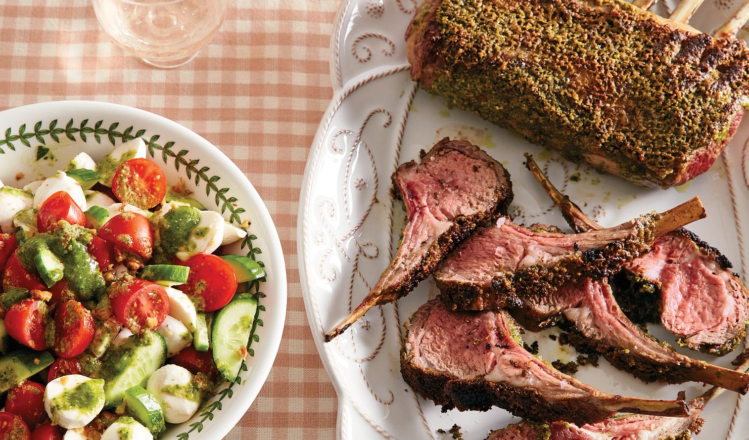 Lamb with Tomato-Mozzarella Salad rack of lamb on a plate next to a tomato, mozarella and cucumber salad with pesto
