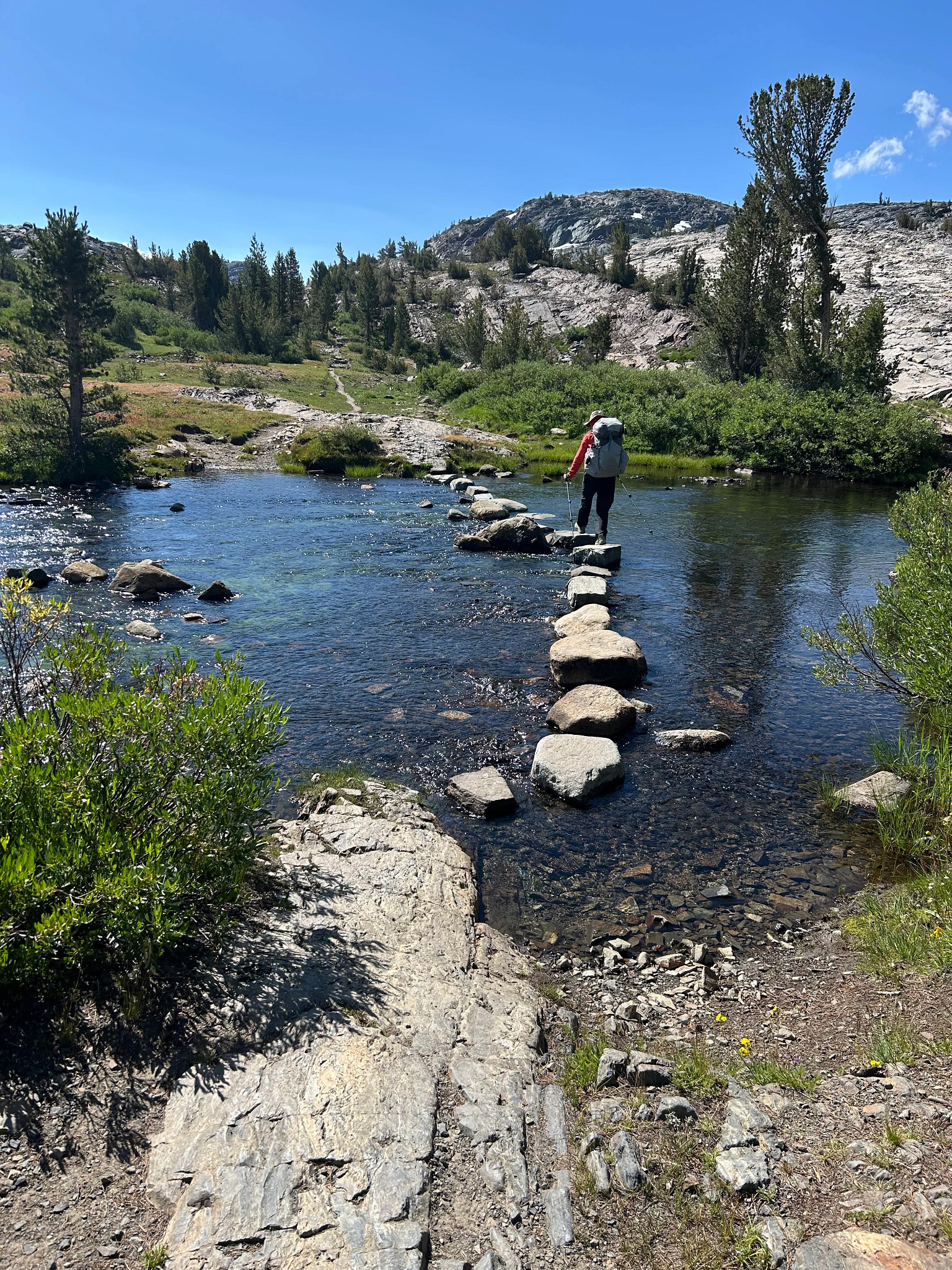 a hiker walking along rocks in the water of the John Muir Trail in California