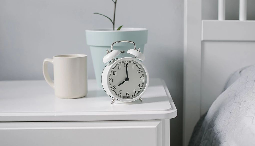 Having a regular sleep-wake schedule is related to better brain health A white alarm clock on a nightstand by a bed