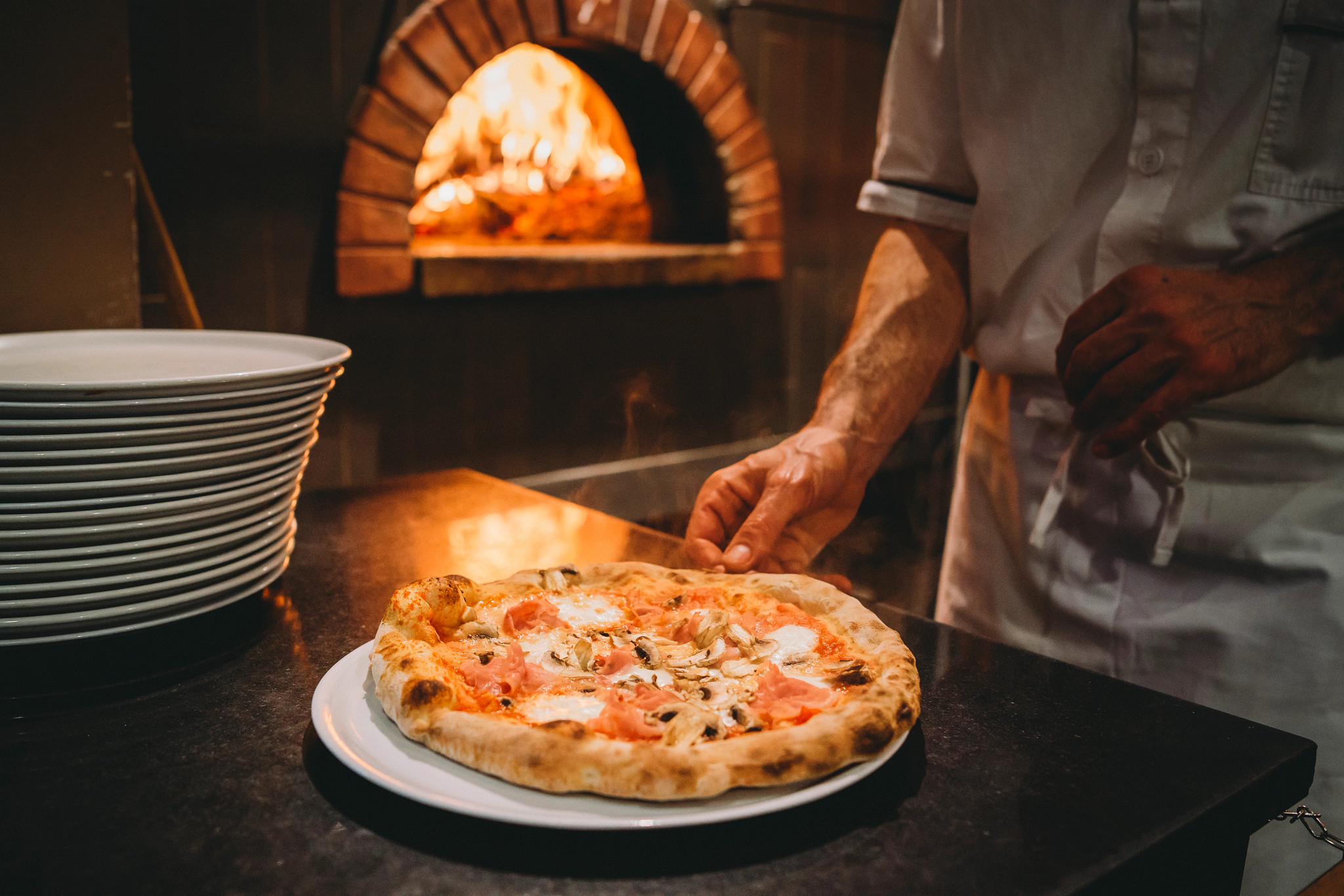 A pizza chef prepares an artisanal pizza at the restaurant, a fire-brick over in the background