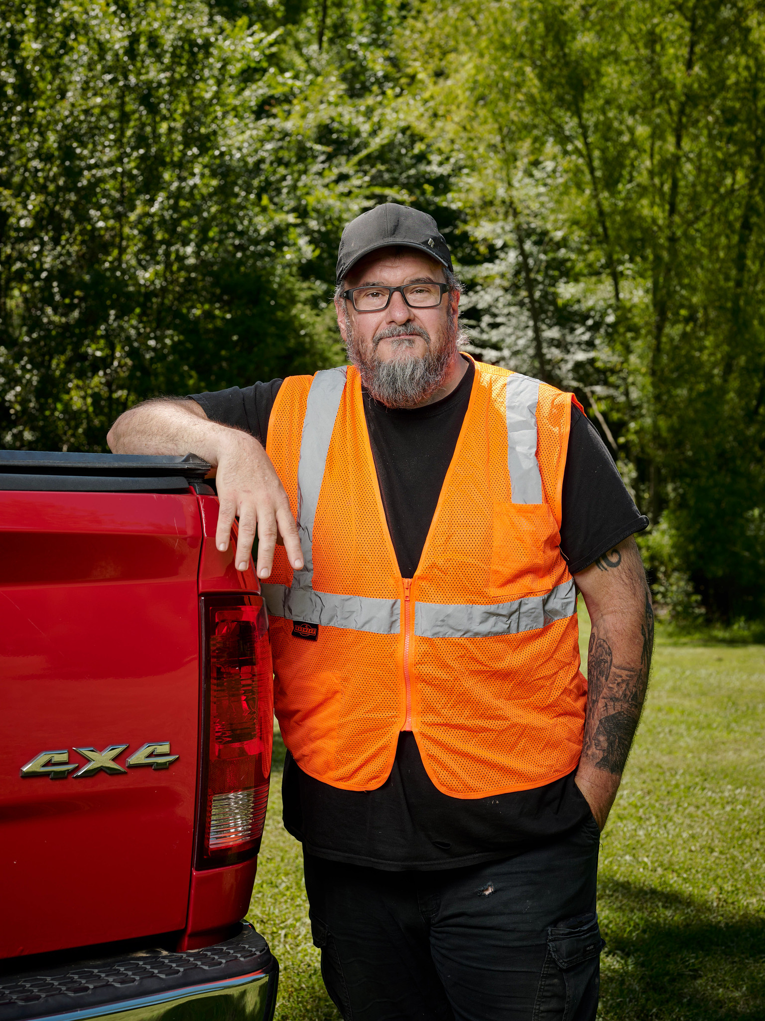 man wearing an orange safety vest stands next to a red pickup truck