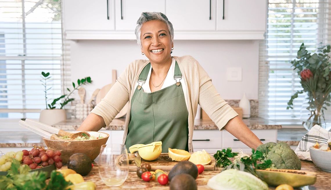 Upping the variety of fruits, veggies, nuts and seeds in your meals helps nourish your gut microbiome A smiling woman posing in front of a lot of vegetables in a kitchen