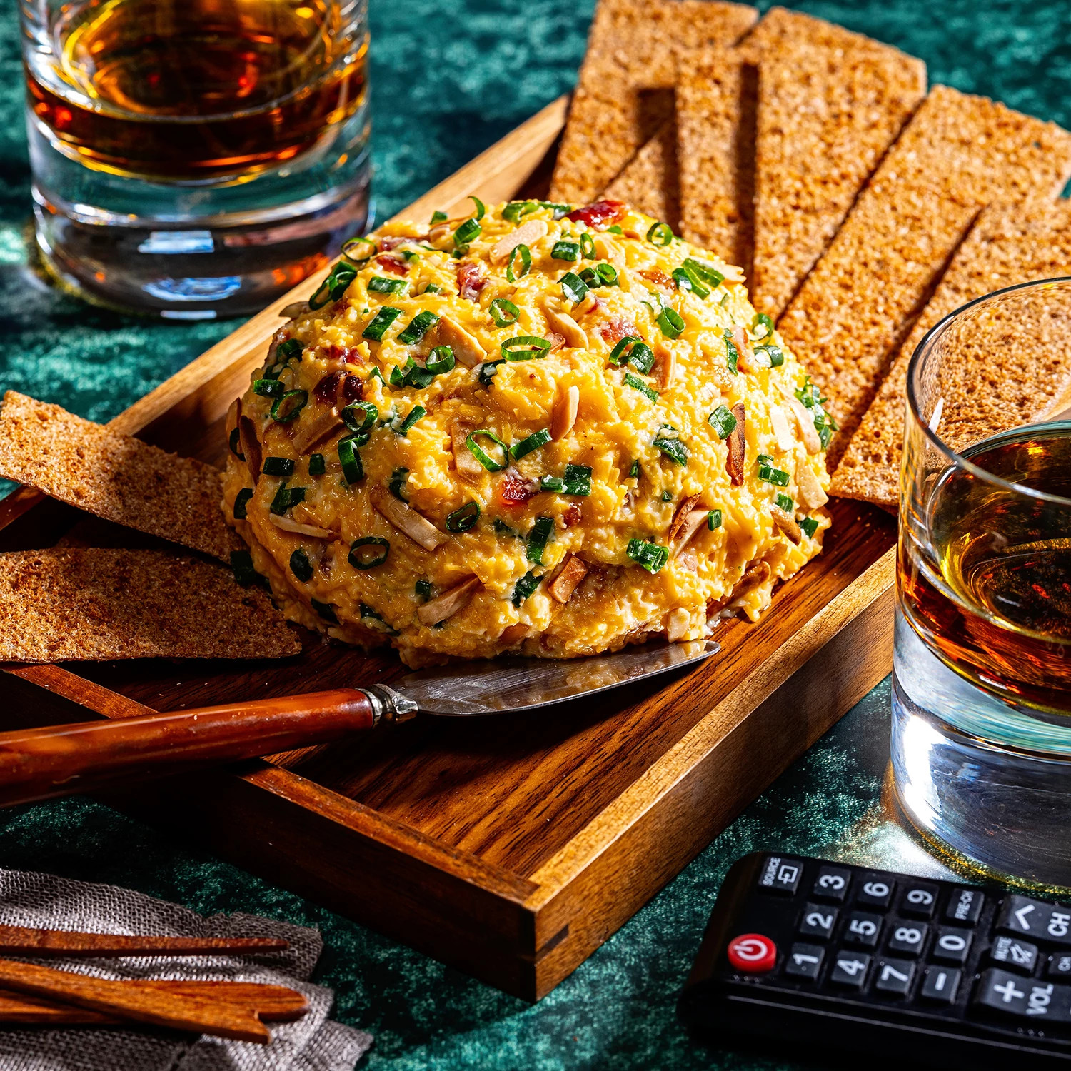 Cheese ball topped with chives and bacon bits served with crackers on a wooden board.