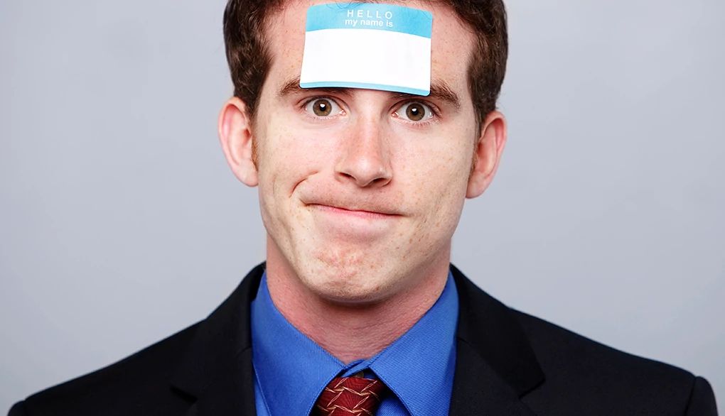 Forgetting names is a common occurrence A man in a suit with a "My name is" sticker on his forehead