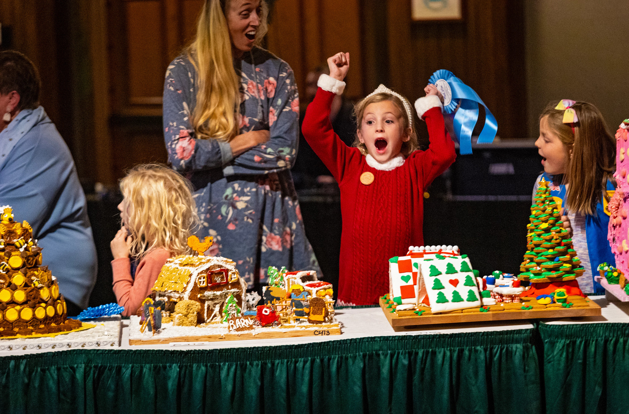 a girl throws her hands up while decorating gingerbread houses