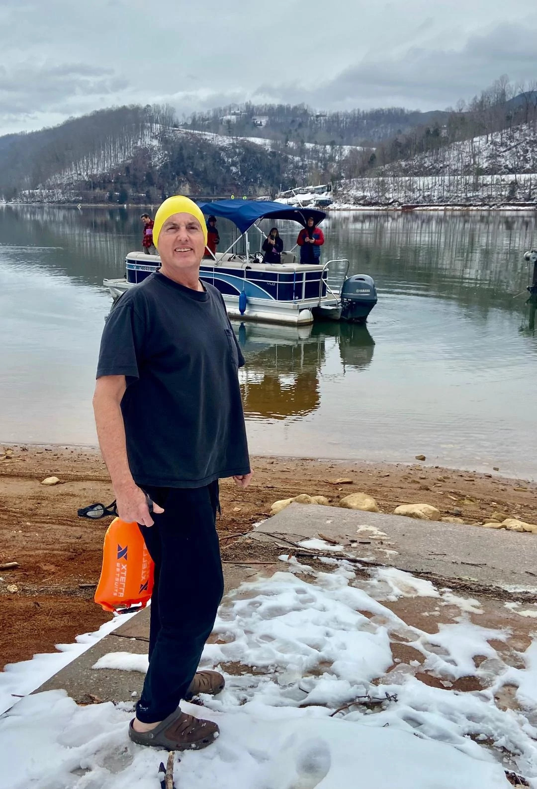 Don Winters in front of body of water, boat in the water, snow on the ground