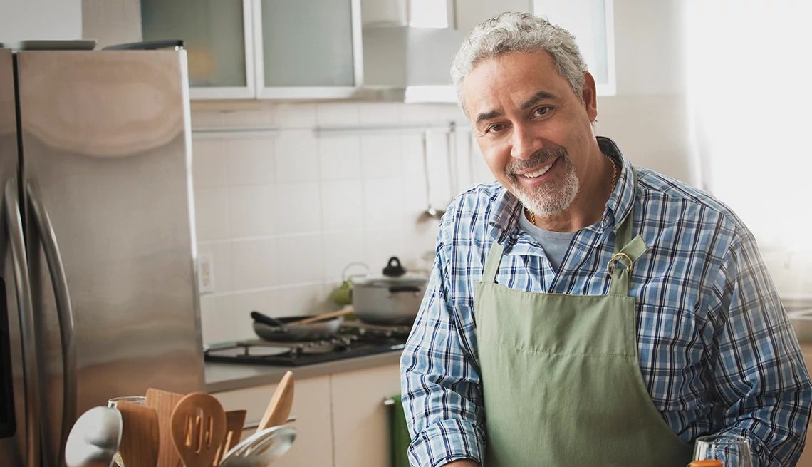 Eating a healthy diet and maintaining a healthy weight is important as you age A man smiling and wearing a chef apron in a home kitchen